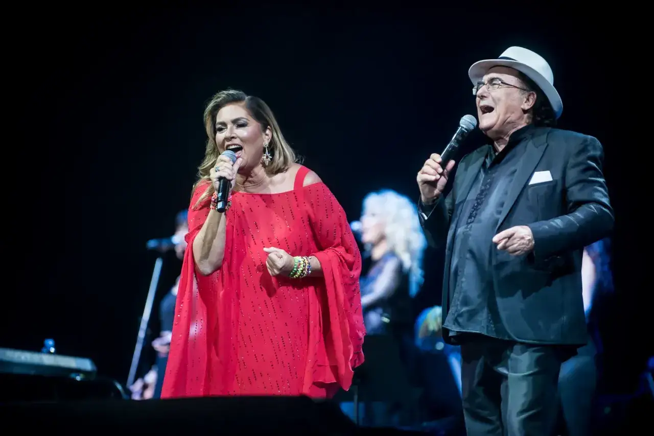 Al Bano i Romina Power na scenie, wokalistka w czerwonej sukni, on w czarnym garniturze i białym kapeluszu.