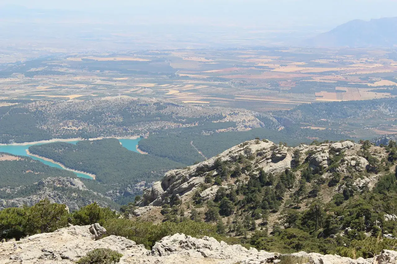 Vistas panorámicas de la sierra de Cazorla, Segura y las Villas, con un embalse turquesa serpenteando entre pinares y campos cultivados al fondo.