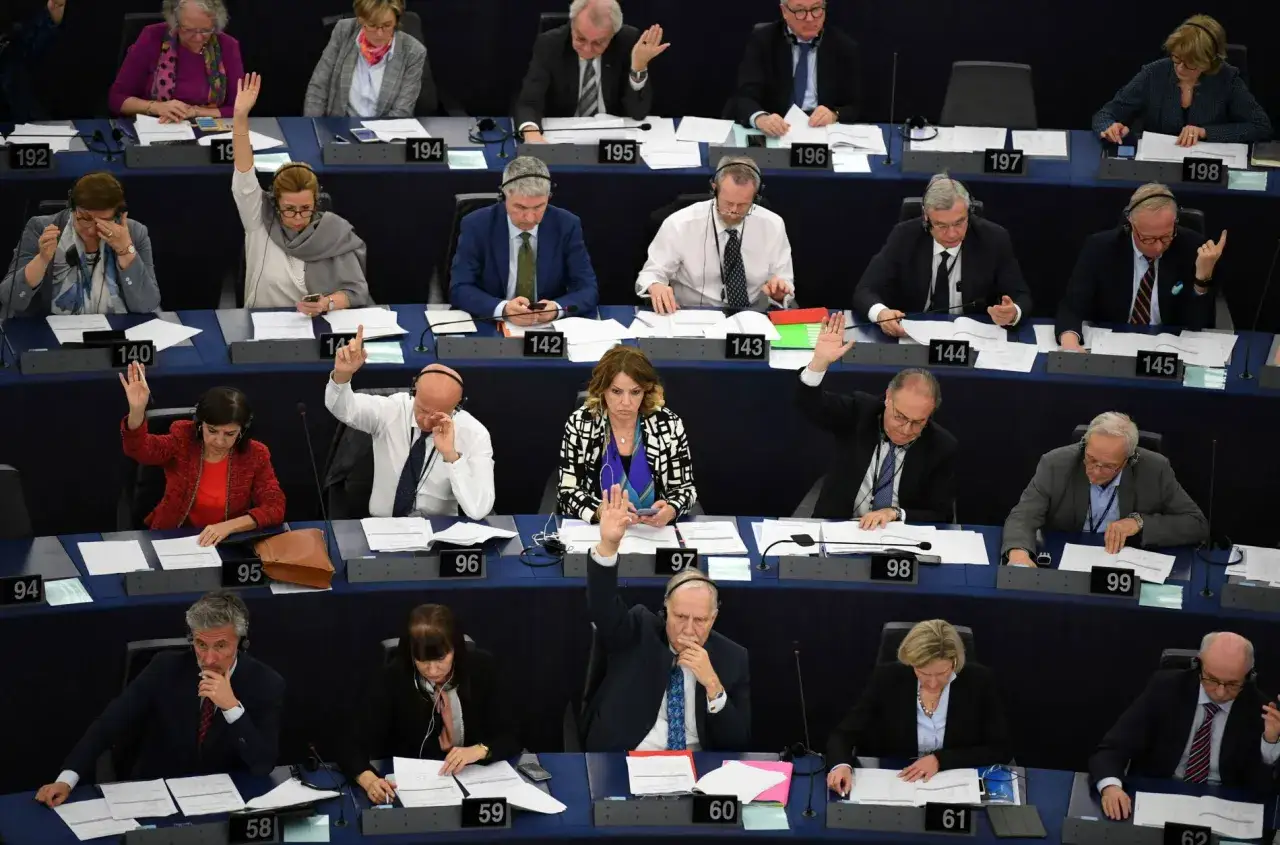 Polscy europosłowie głosują w Parlamencie Europejskim. Widać ich listę i podniesione ręce.