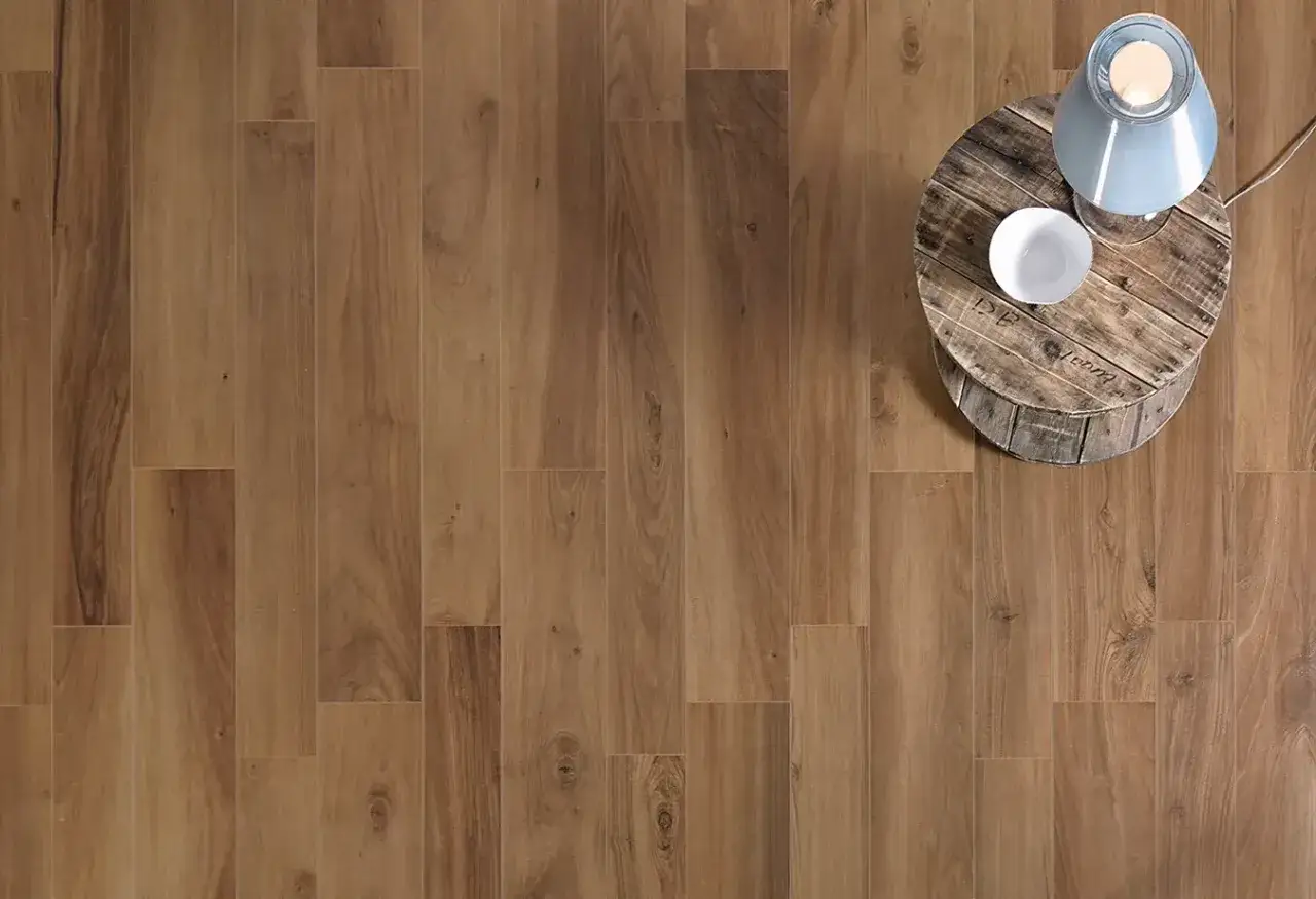 Posa pavimento gres effetto legno, con un tavolino rustico in legno e una lampada.
