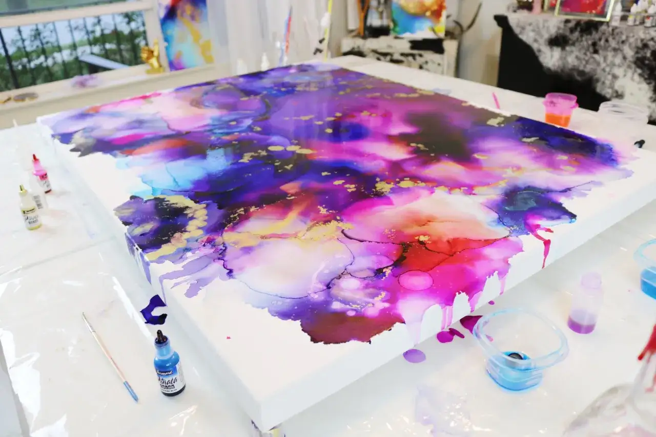 Une toile abstraite aux couleurs vives, violettes, roses et bleues, avec des touches dorées. L'encre alcool sur toile coule et crée des formes organiques.