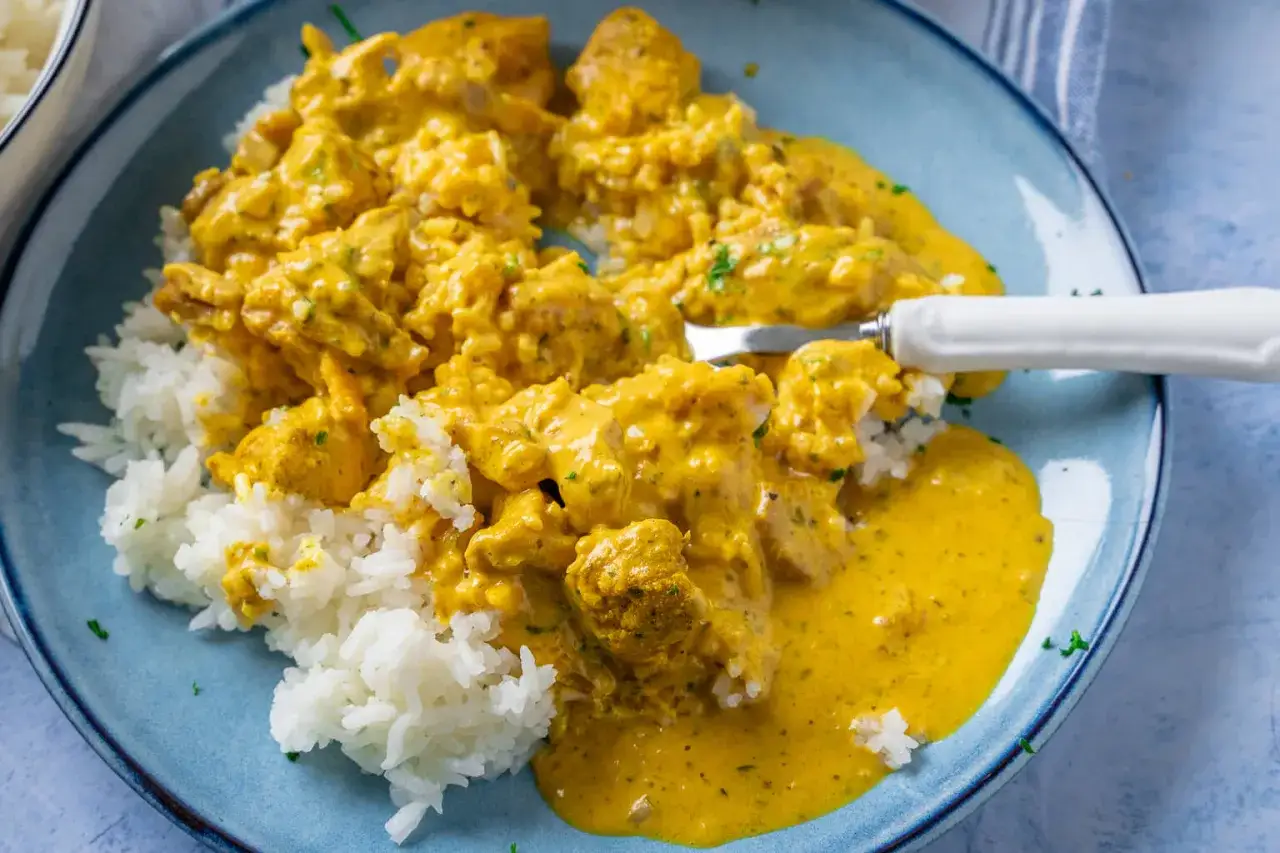 Ein Teller mit Reis und cremigem Curry Geschnetzeltes Rezept. Eine Gabel steckt in dem Gericht.