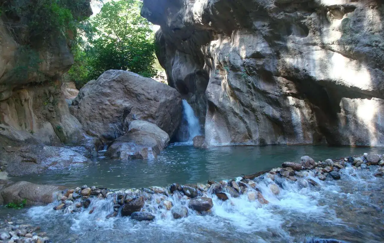 Cascada y poza natural en los canales de Padules, rodeada de rocas y vegetación exuberante.