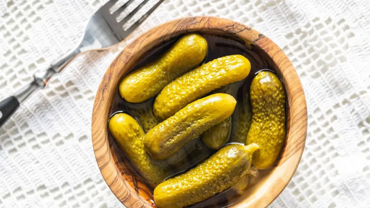 Schon eingelegt nach Omas Rezept: saure Gurken in einer Holzschale, bereit zum Genuss. Eine Gabel liegt daneben.