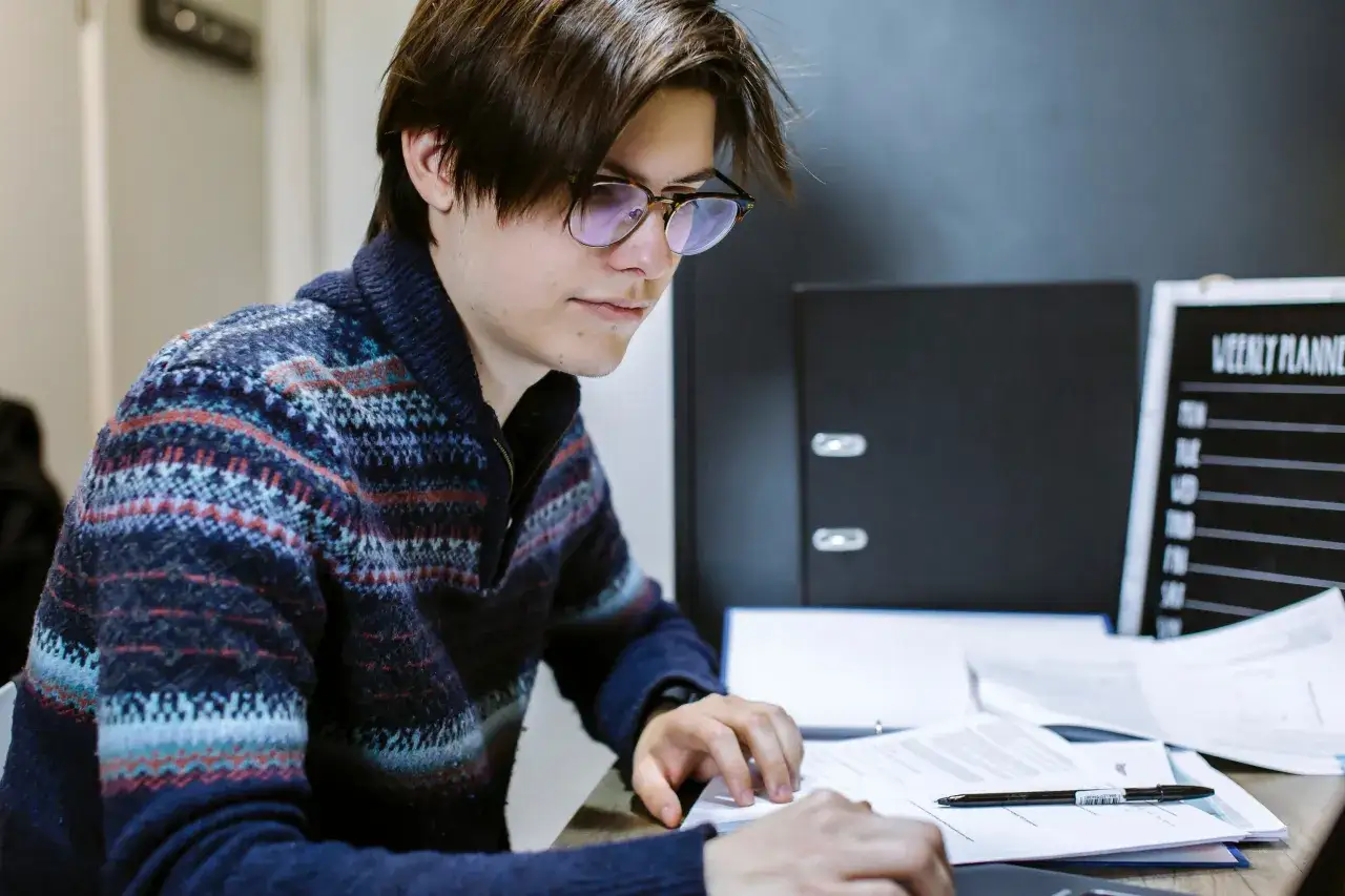 Young man studying for his public administration degree online, surrounded by papers and a weekly planner.