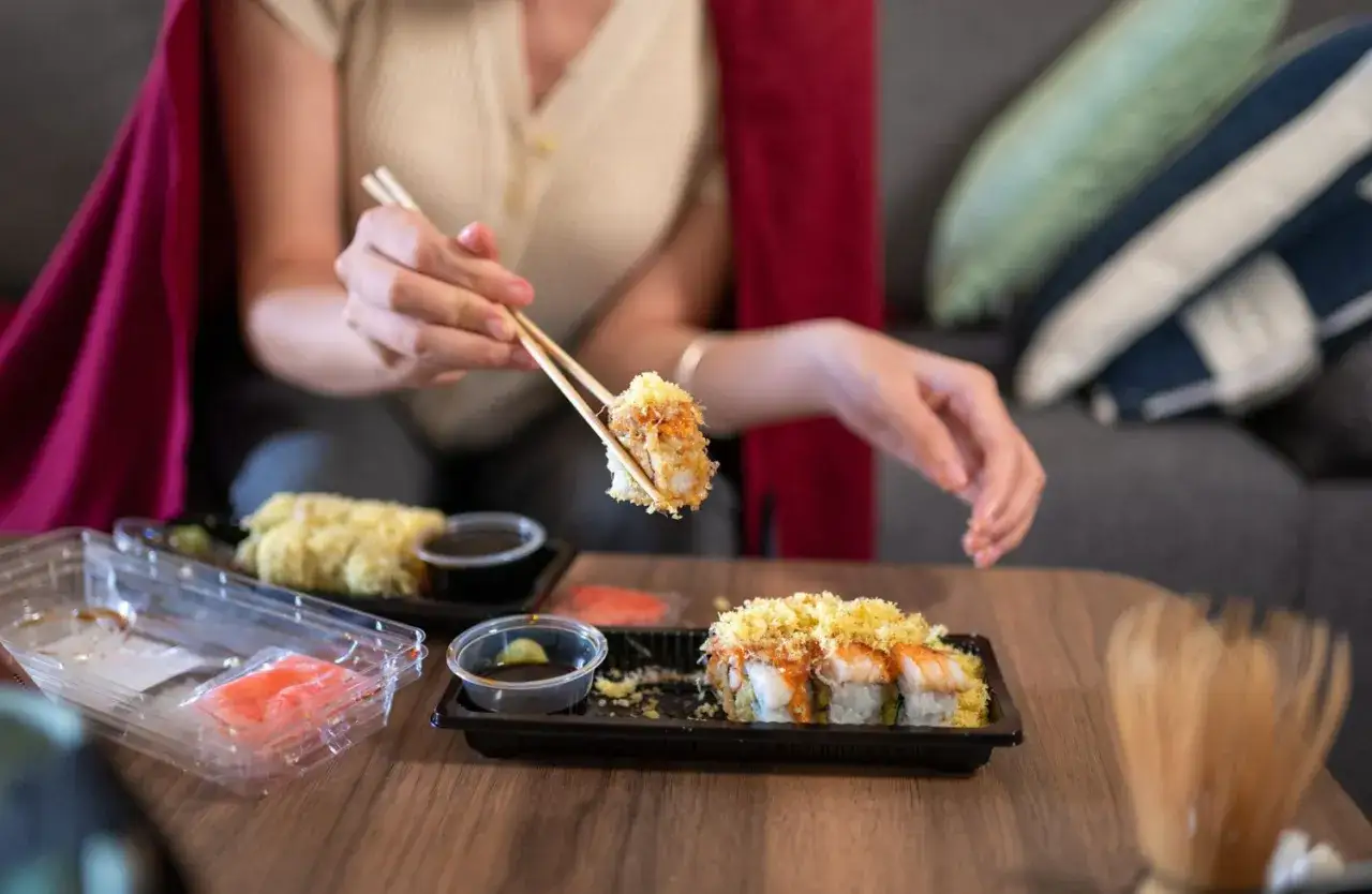 En gravid kvinna njuter av sushi hemma. Hon håller en bit sushi med ätpinnar.