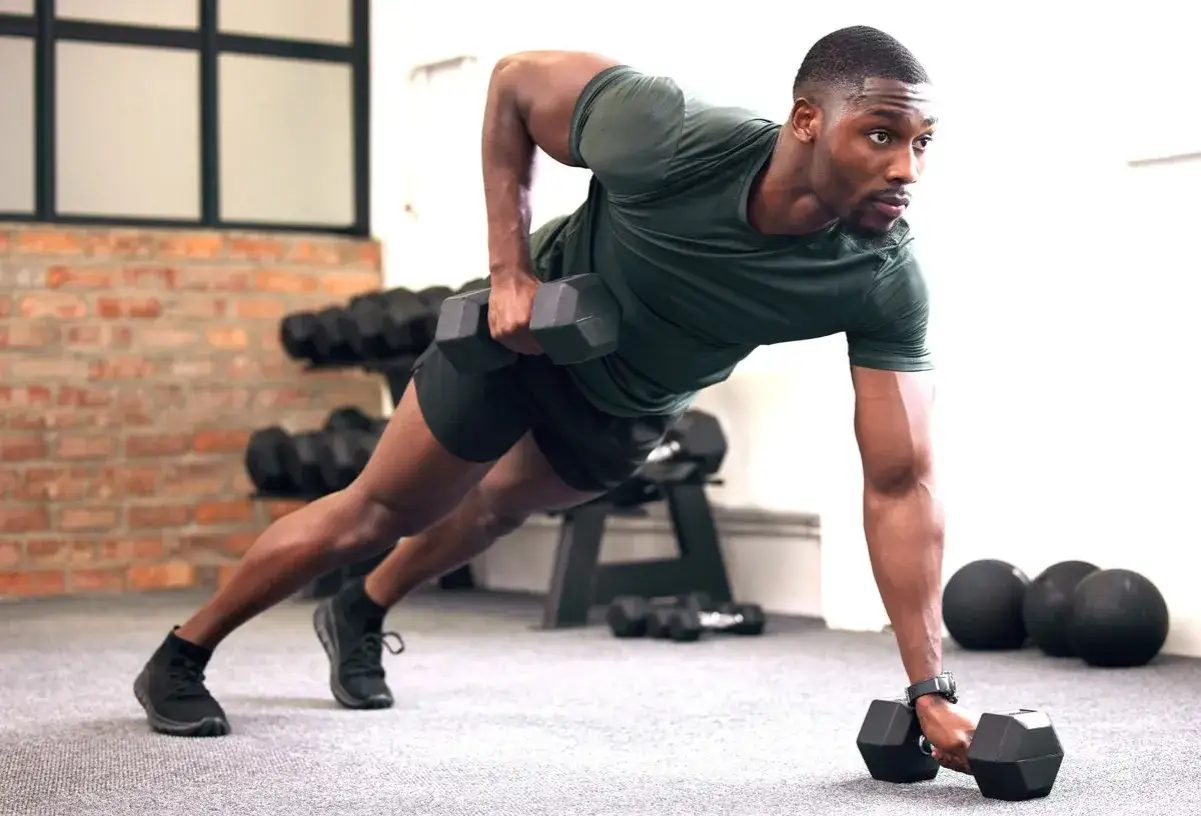 Mann in Plank-Position mit Hanteln, trainiert seinen Körper für stabi Training.