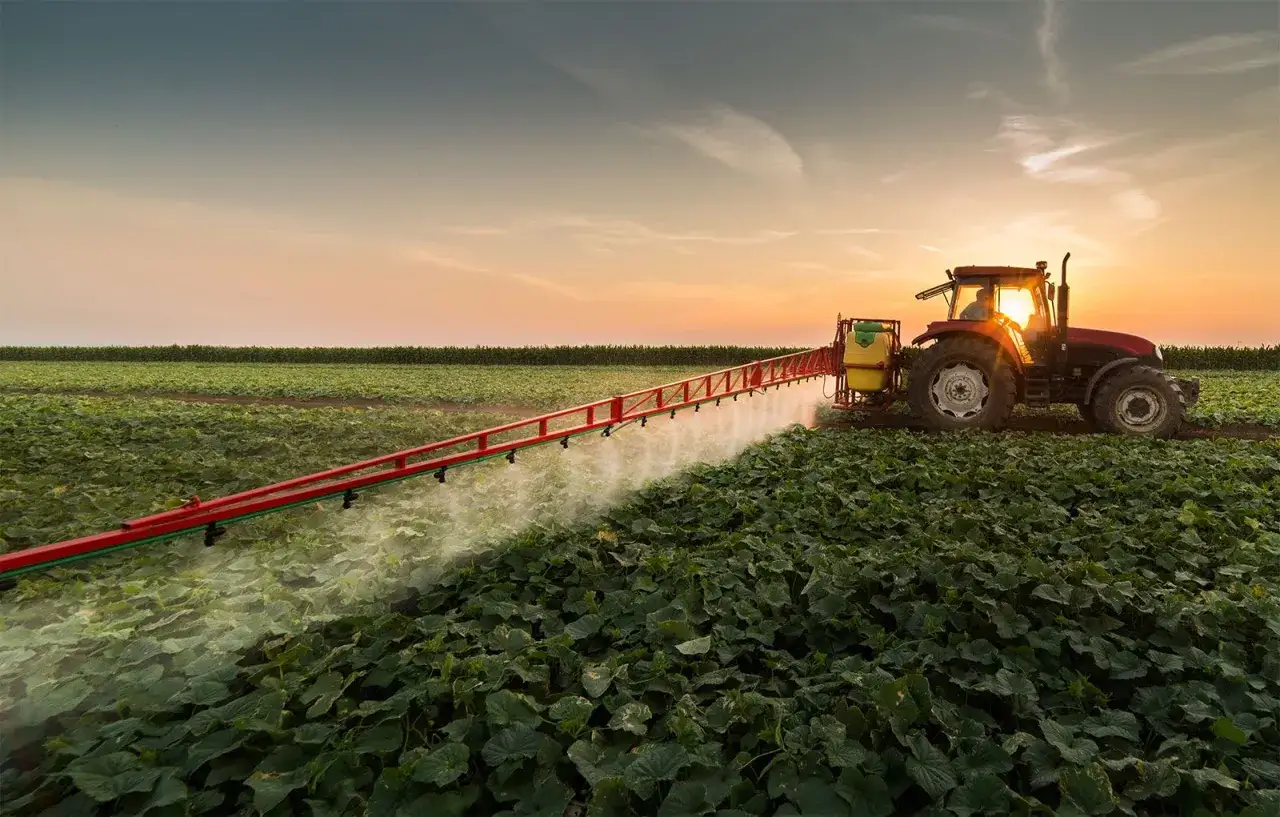 A red tractor with a sprayer attachment cultivates a field at sunset. These implements are essential for modern farming.