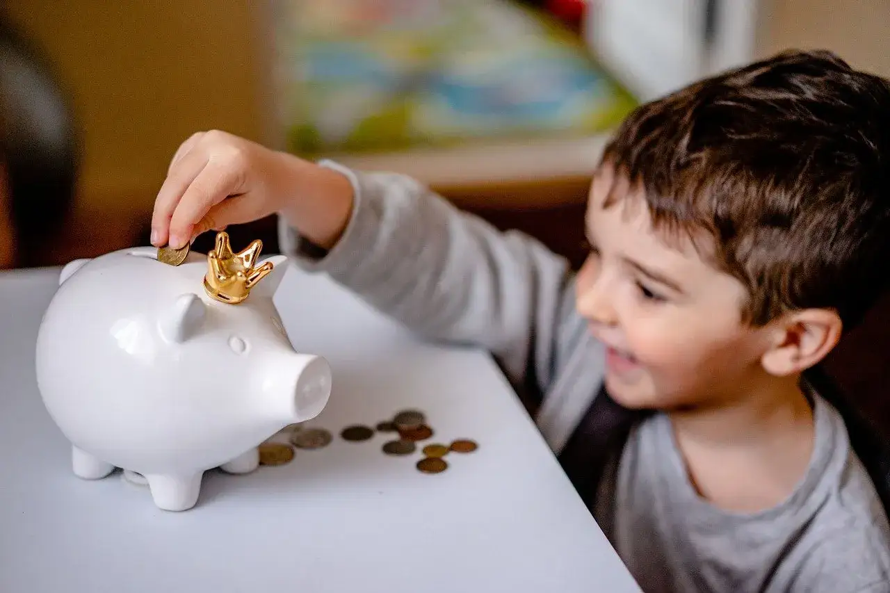 Chłopiec wkłada monetę do świnki skarbonki z koroną. Uczy się oszczędzać kieszonkowe dla dziecka.