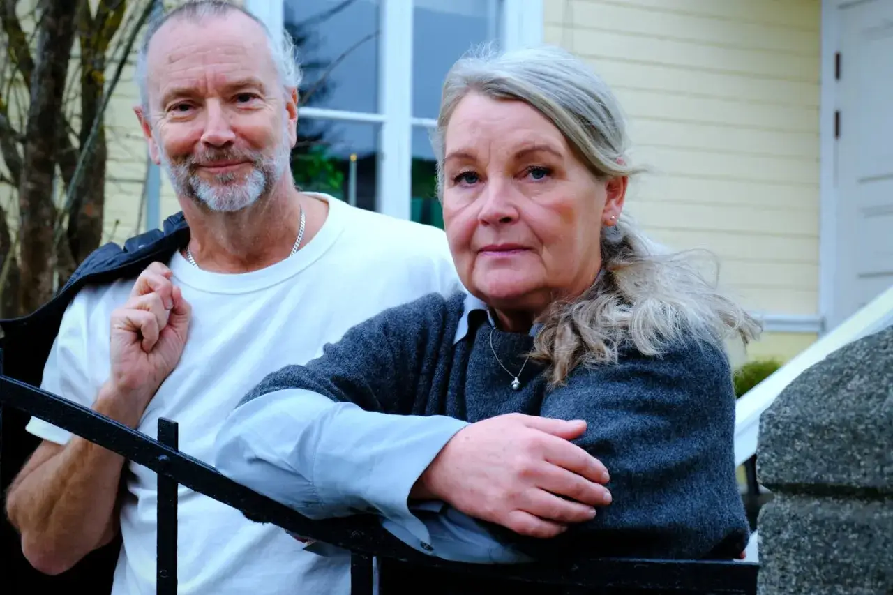 Ett äldre par, Ola Liljedahl och hans fru, poserar framför ett gult hus.