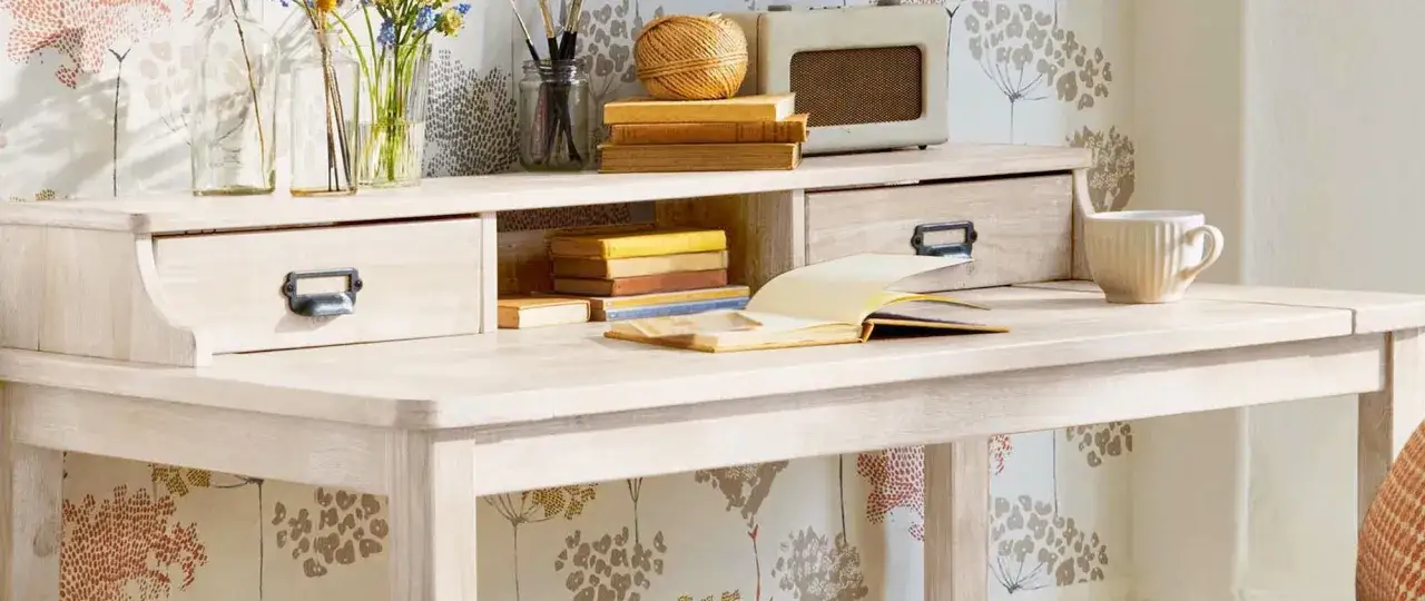 Scrivania in legno chiaro, perfetta per chi vuole imparare come verniciare un mobile da marrone a bianco. Libri, tazza e radio vintage completano la scena.