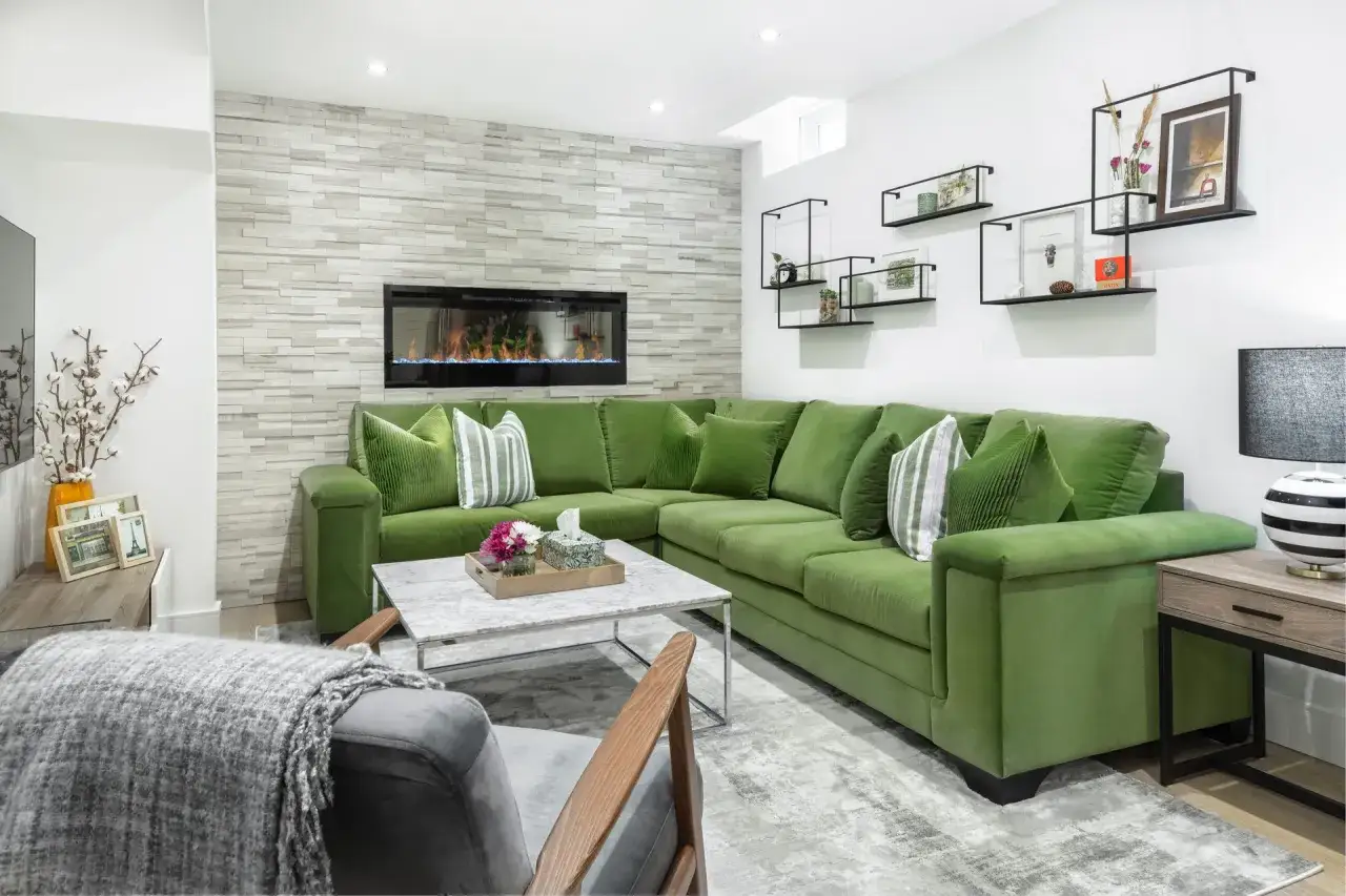 A bright, modern living room with a large green sectional sofa, a fireplace, and decorative shelves. This is not a dark basement.