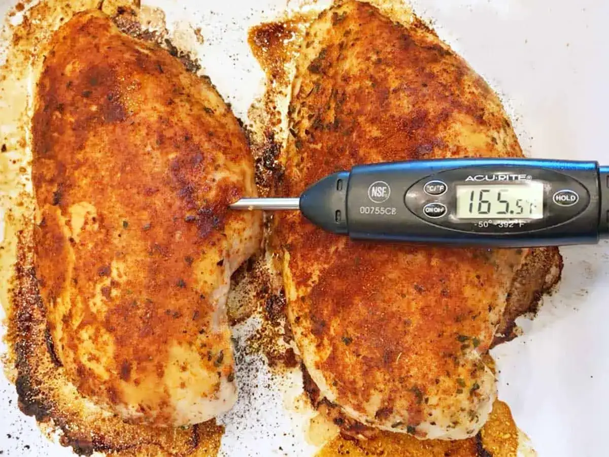 Zwei gew&uuml;rzte H&auml;hnchenbrustfilets auf einem Blech. Ein Fleischthermometer zeigt die pollo fino kerntemperatur von 165,5&deg;F an.