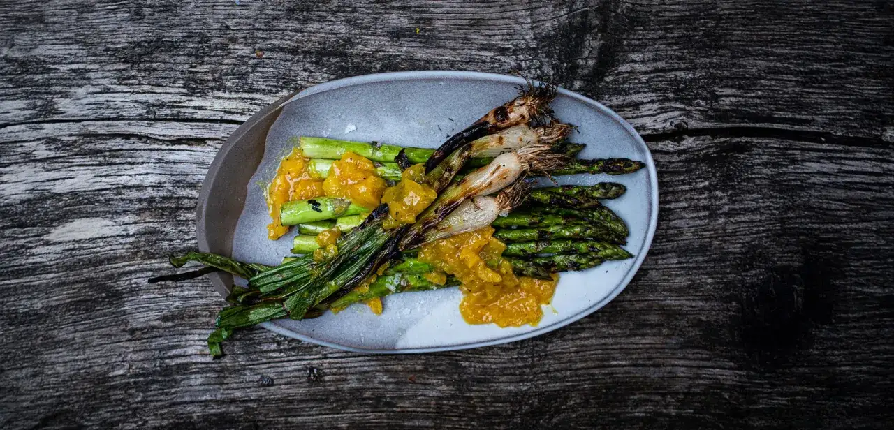 Grillspargel mit einer leuchtend gelben Sauce auf einem rustikalen Holztisch. Die Spargelstangen sind leicht gebräunt und mit zarten Röstspuren versehen.