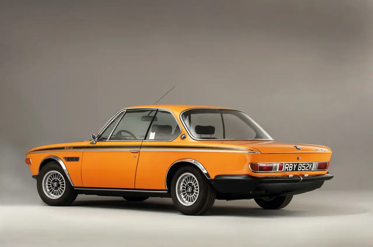 En orange BMW E9, en klassisk coupé med svarta detaljer och kromade fälgar, står redo för en tur.