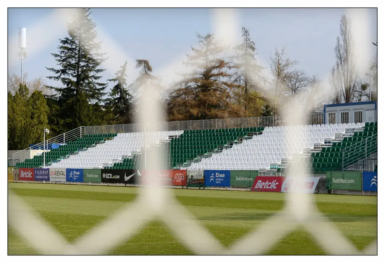 Puste trybuny stadionu Warty Poznań czekają na kibiców. Zielono-białe krzesełka i murawa gotowe na kolejny mecz.