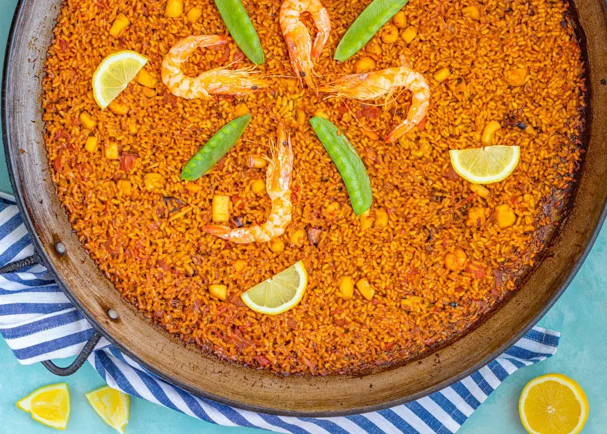Arroz a banda receta: paella de marisco con gambas, guisantes y lim&oacute;n en una paellera.