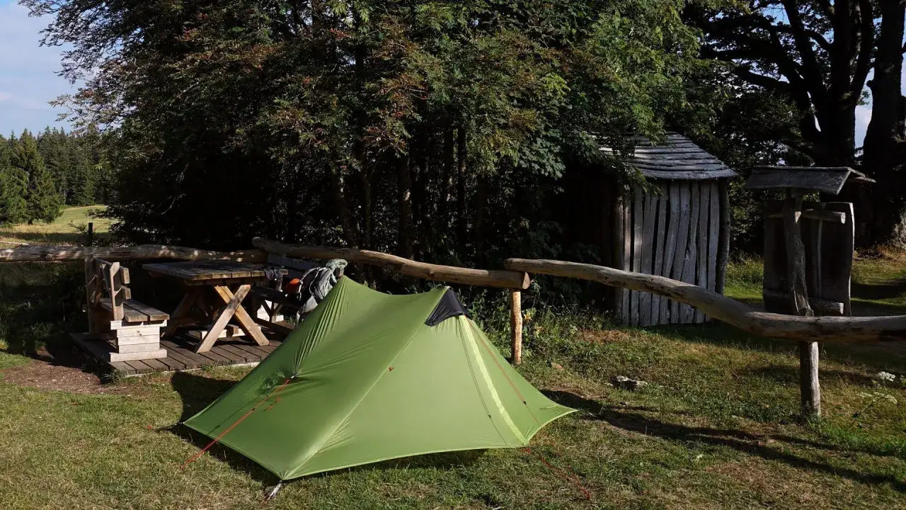 Gr&uuml;nes Zelt und Holztisch laden zum biwakieren Deutschland ein. Im Hintergrund eine kleine Holzh&uuml;tte.