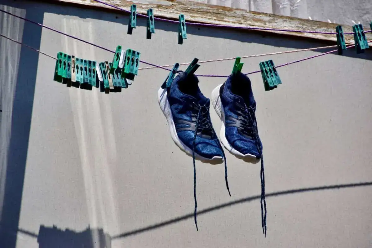 Blaue Turnschuhe trocknen an einer W&auml;scheleine, befestigt mit gr&uuml;nen Klammern.