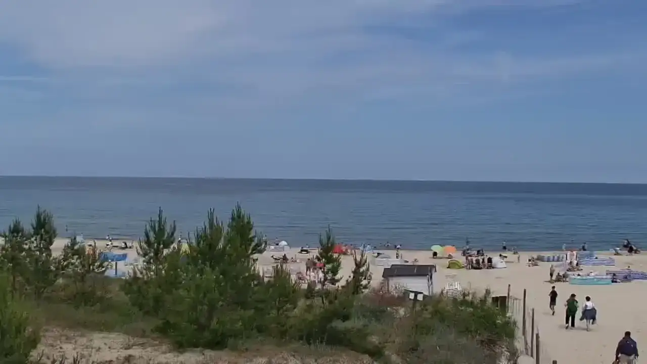 Plaża w Karwi tętni życiem. Ludzie odpoczywają pod kolorowymi parasolami, a morze spokojnie faluje.