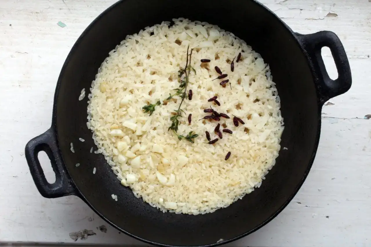 Jak ugotować ryż? W czarnym garnku gotowy ryż z czosnkiem, gałązką tymianku i suszonymi papryczkami chili.