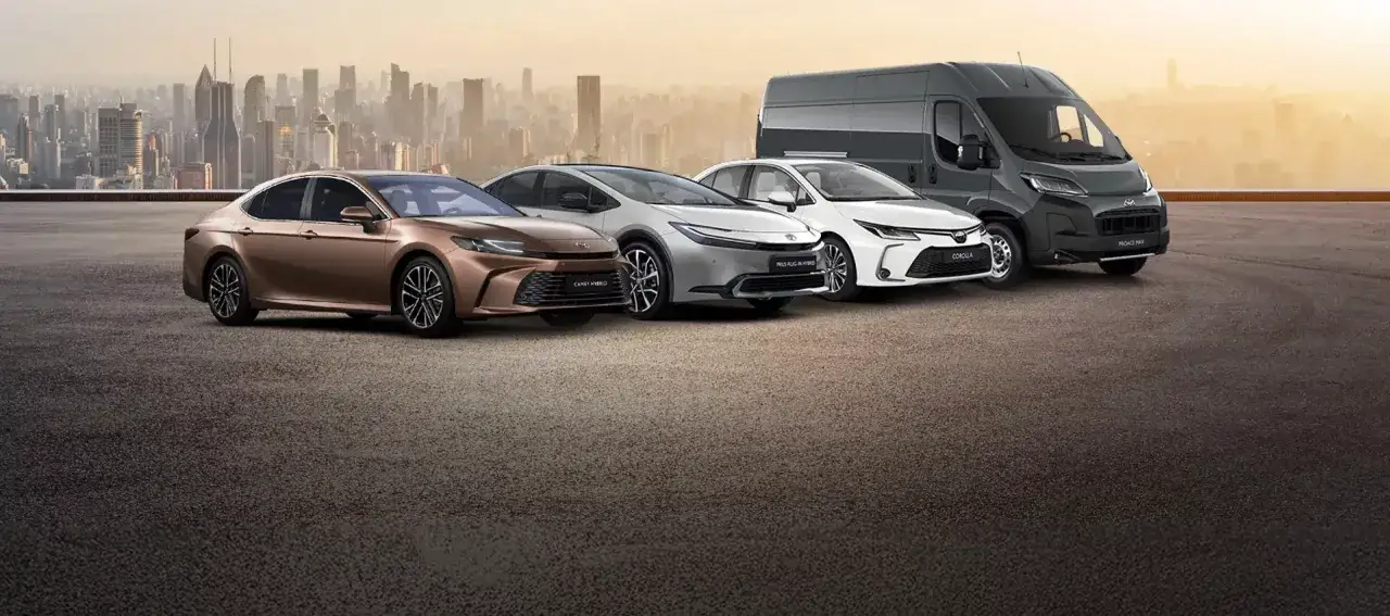 Różnorodne modele Toyota: brązowa Camry Hybrid, srebrny Prius Plug-in Hybrid, biała Corolla i szary Proace Max na tle miasta.