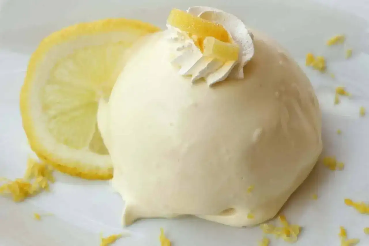 Una soffice delizia al limone, guarnita con panna e scorzette, accanto a una fetta di limone.