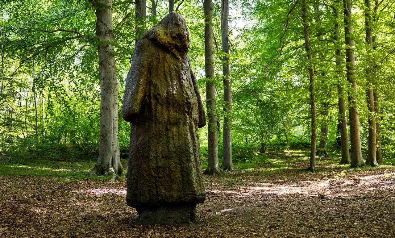 En mystisk figur står i en lummig skog. En del av prinsessan Estelles skulpturpark, där naturen möter konst.