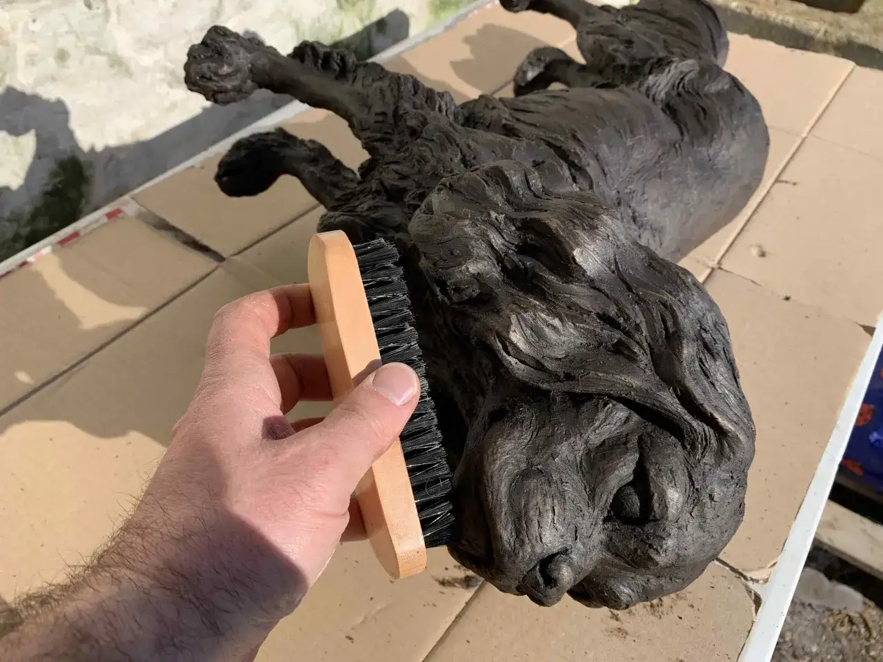 Mano cepillando una escultura de bronce de un perro, restaurando su brillo.