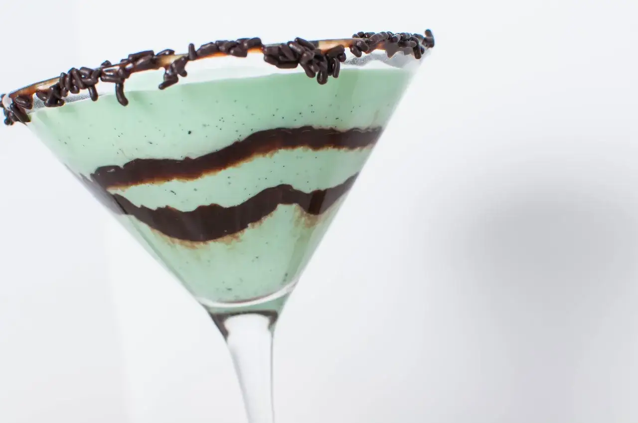 Gr&ouml;n, kr&auml;mig Grasshopper drink med chokladstr&ouml;ssel p&aring; kanten och choklads&aring;s virvlad inuti.
