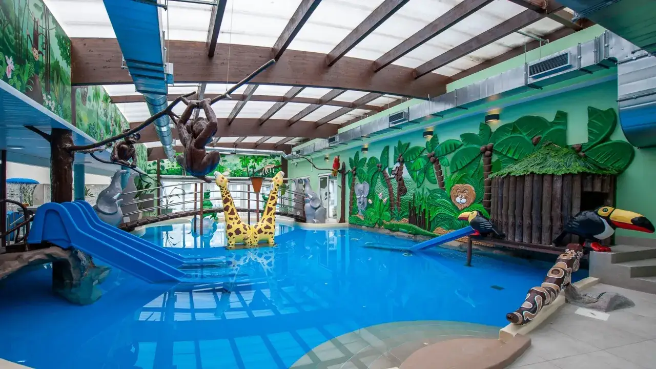Wesoły aquapark Pobierowo z basenem, zjeżdżalniami i dekoracjami w dżungli: małpy, żyrafy, słonie, lew i ptaki.