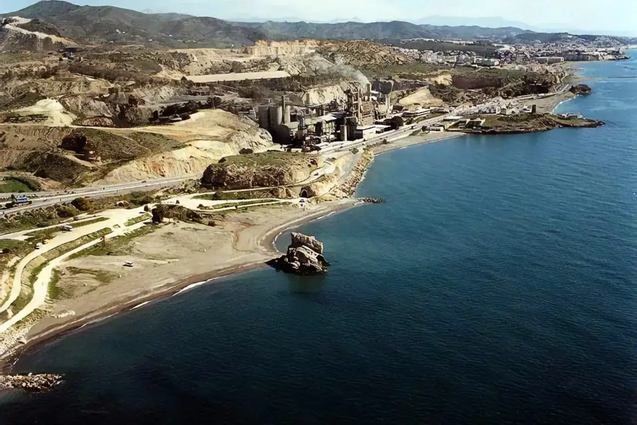 Vista aérea de la playa Peñón del Cuervo con una cantera y una fábrica en la costa.
