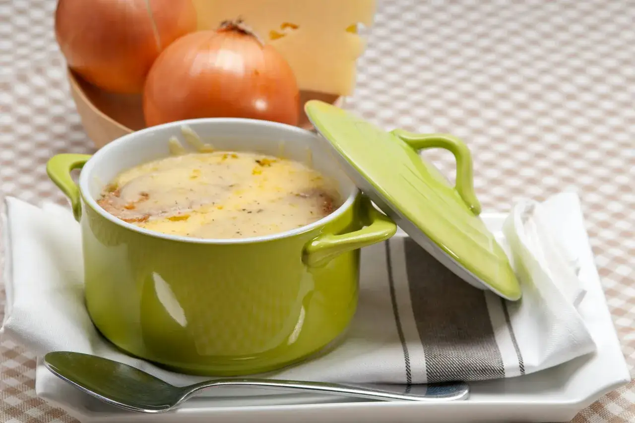 Herzhaftes Zwiebelsuppe Rezept in einem grünen Topf, mit Käse überbacken. Dazu Zwiebeln und Käse.