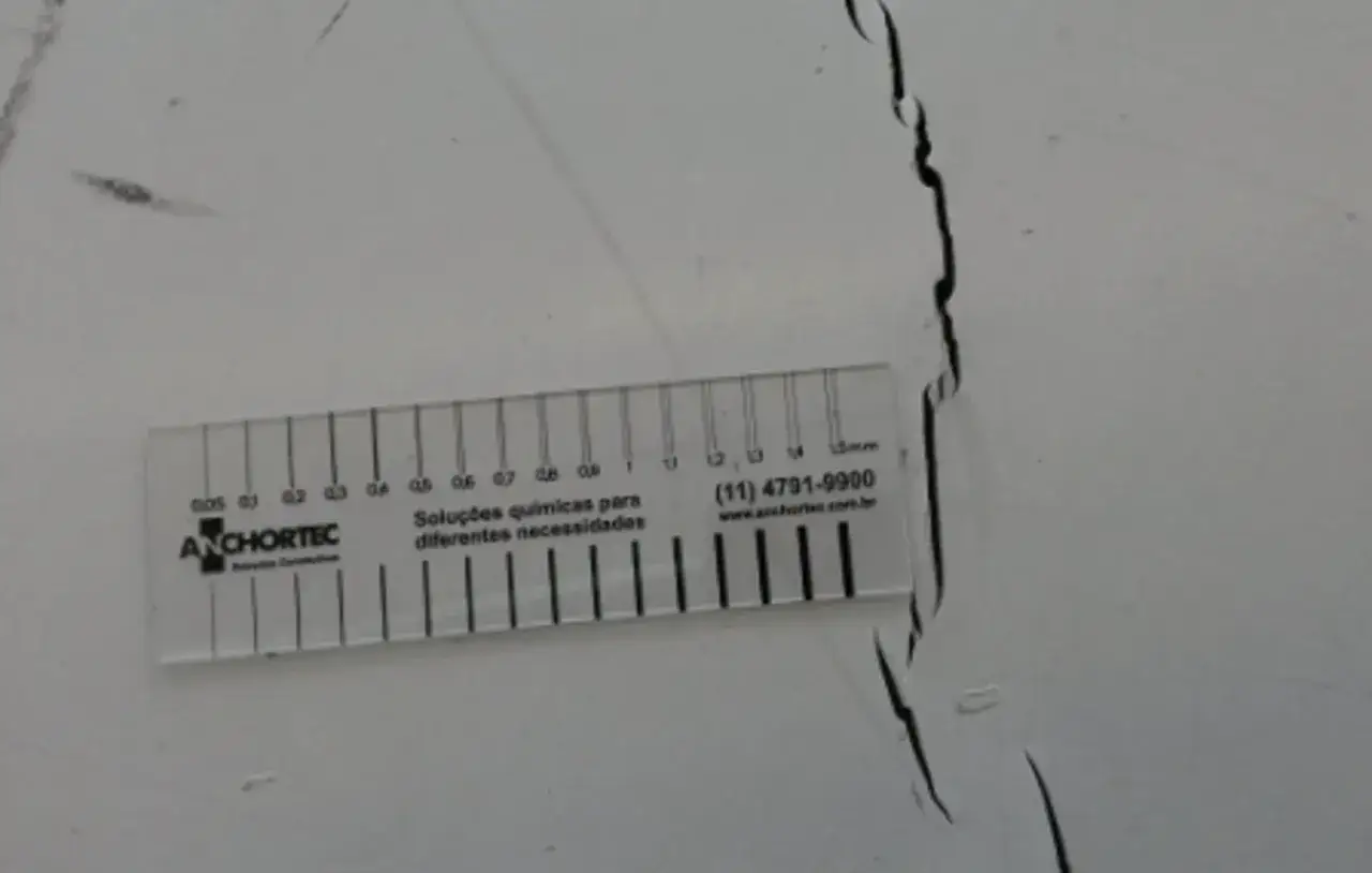 Une règle mesure une fissure dans un chape avant carrelage. La fissure est noire et irrégulière.