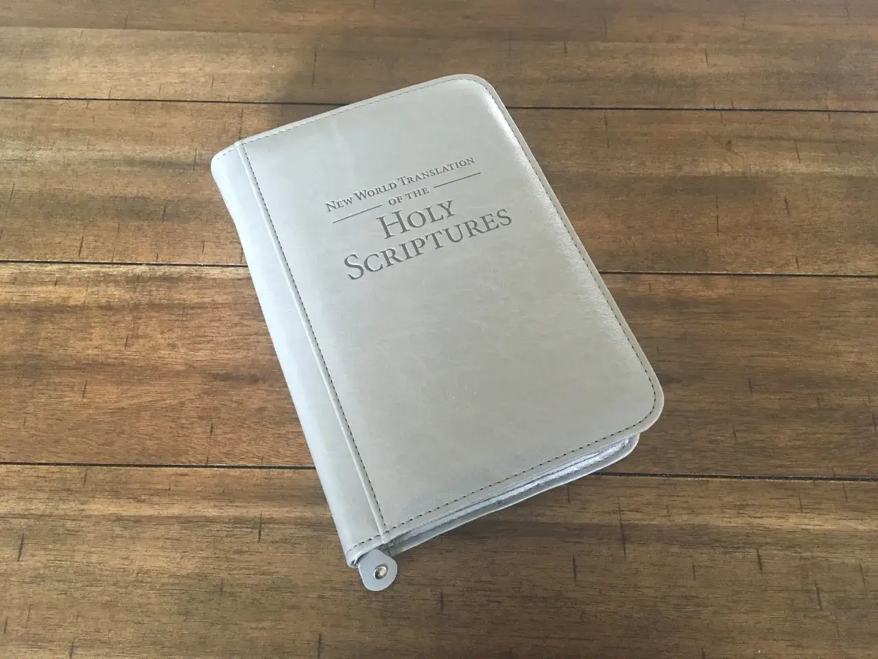 Jasnoszara okładka Biblii Nowego Świata leży na drewnianym blacie.