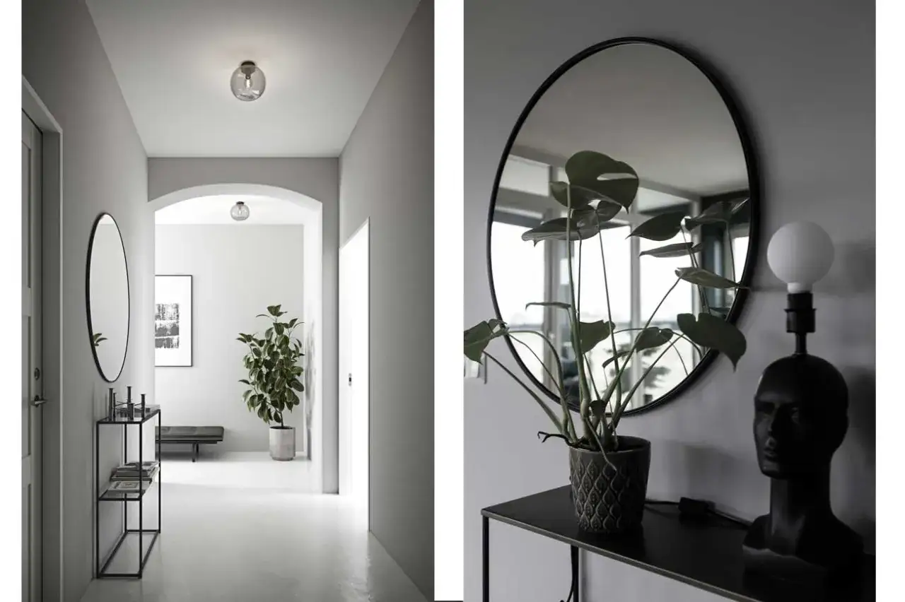En stilren hall med en rund spegel som ger spegel hall inspiration. En stor gr&ouml;n v&auml;xt och en unik lampa i form av ett huvud.