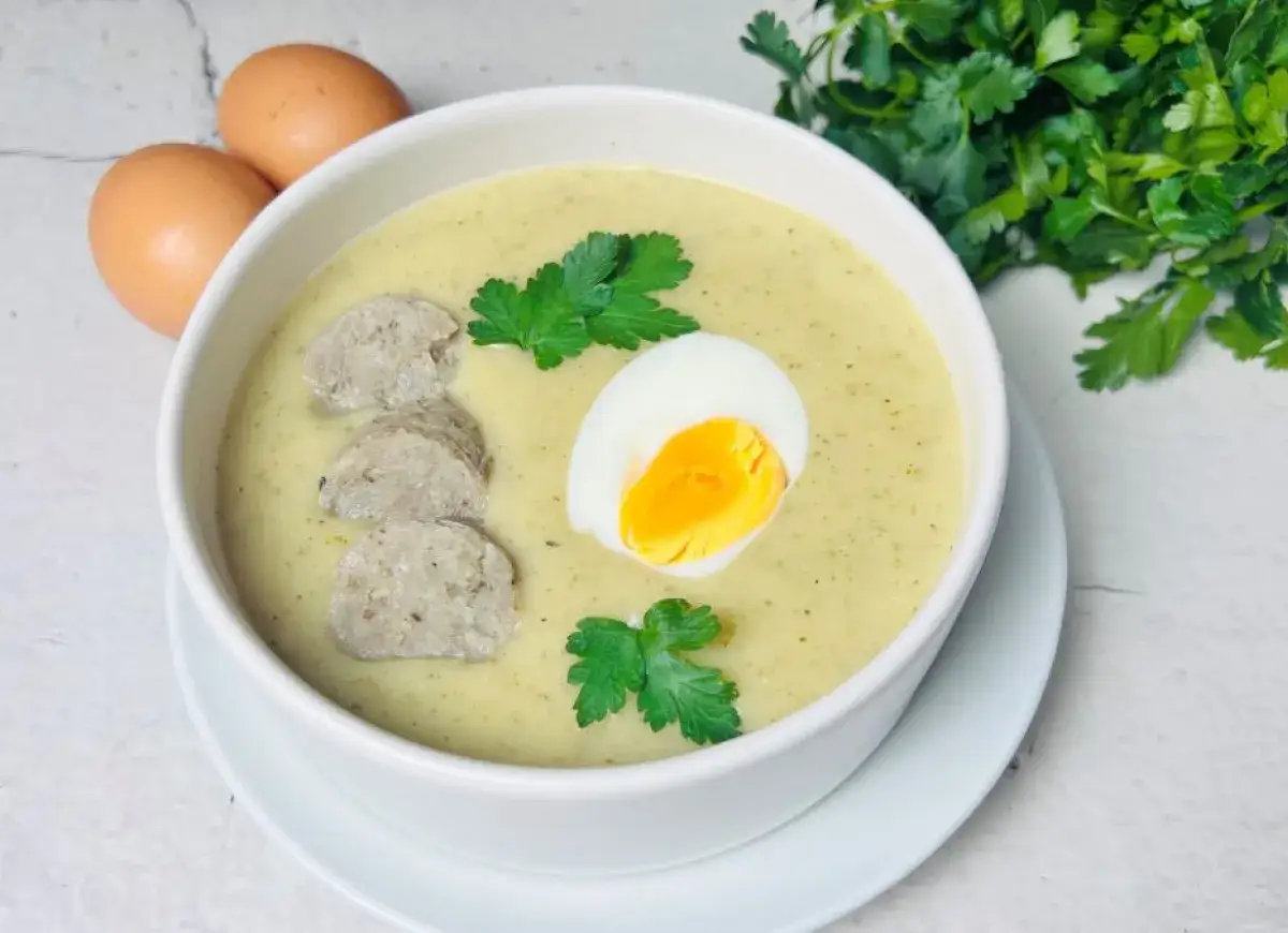 Aromaticzna tradycyjna zupa chrzanowa z jajkiem i kiełbasą, udekorowana natką pietruszki. Obok leżą dwa jajka.
