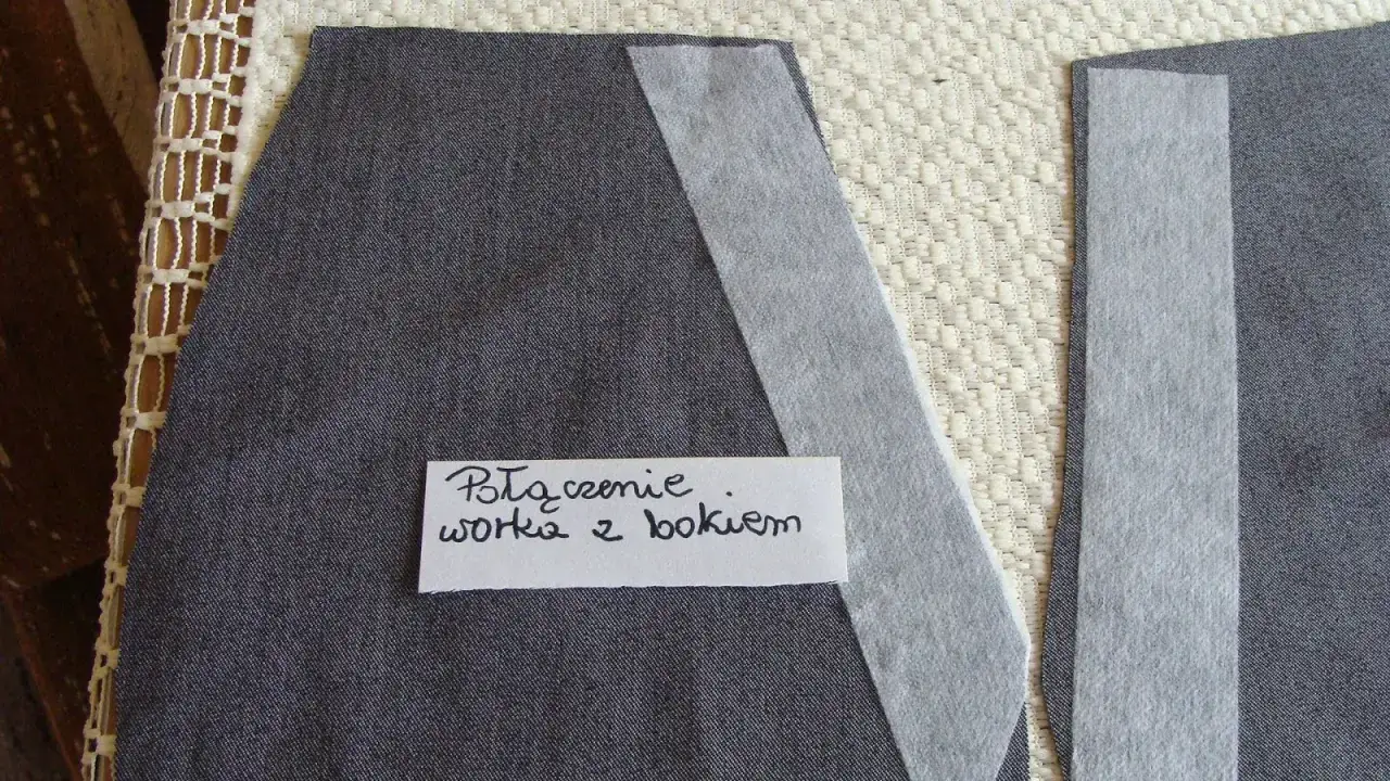 Szare fragmenty materiału, przygotowane do szycia spodni. Na jednym z nich widoczny napis: 