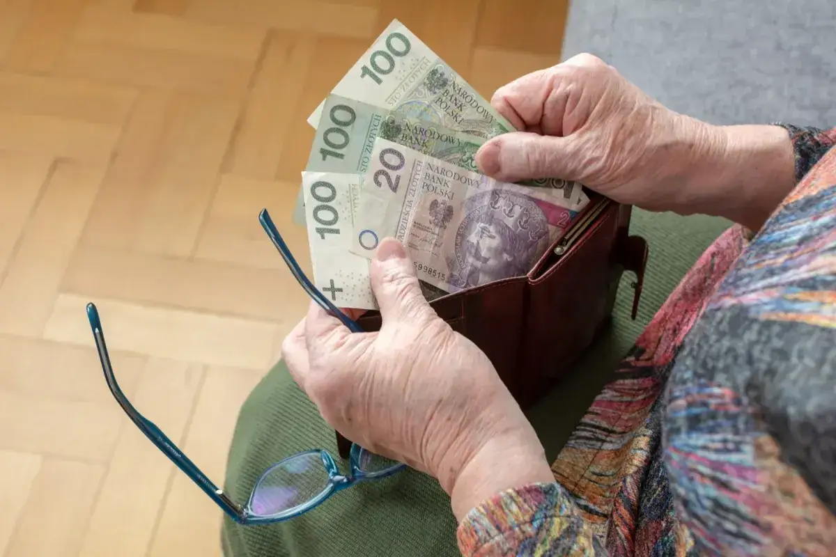 Dłoń starszej osoby wkłada pieniądze do portfela. Zastanawiasz się, w jakim miesiącu najlepiej przejść na emeryturę?