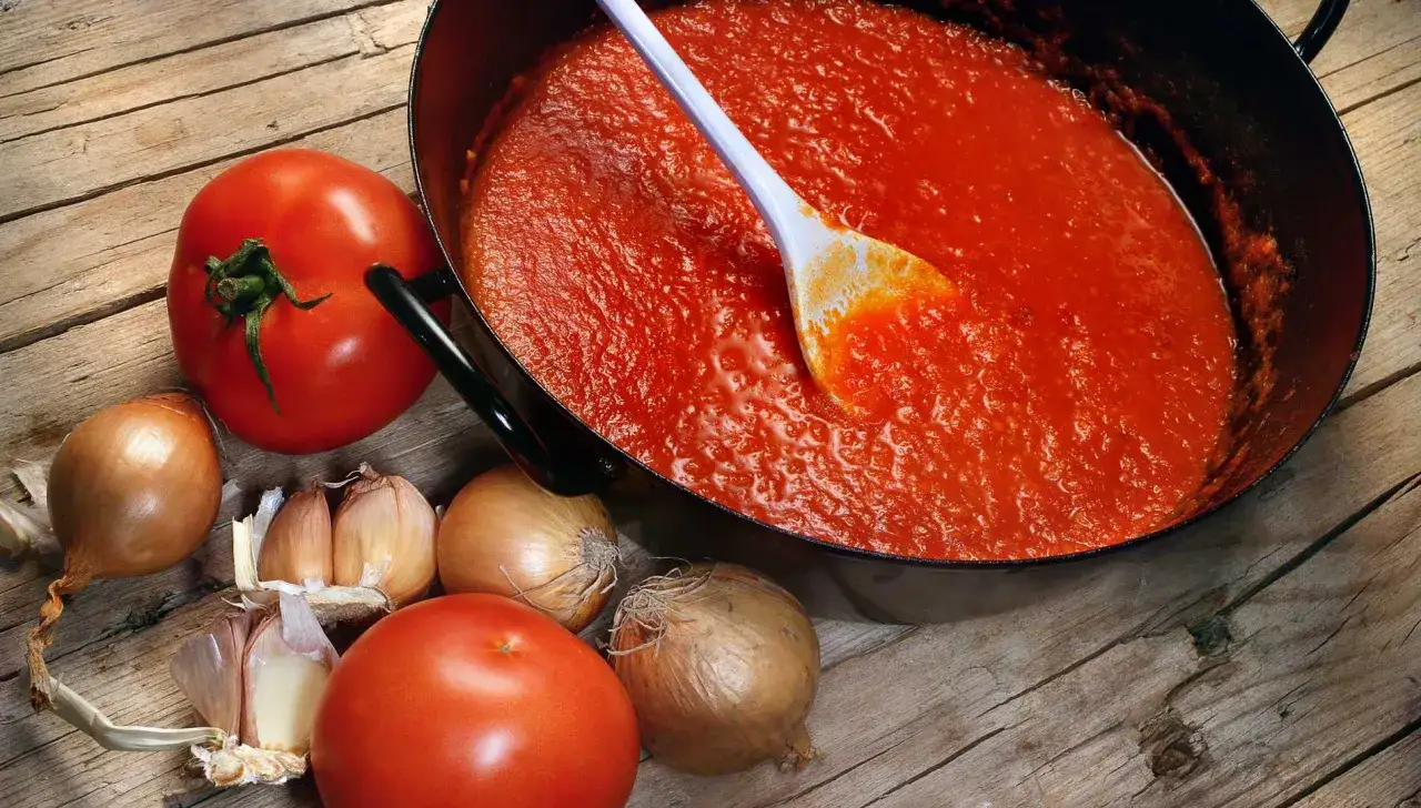 En kastrull med mustig tomats&aring;s, omgiven av f&auml;rska tomater, l&ouml;k och vitl&ouml;k. Perfekt f&ouml;r att g&ouml;ra en klassisk tomats&aring;s.