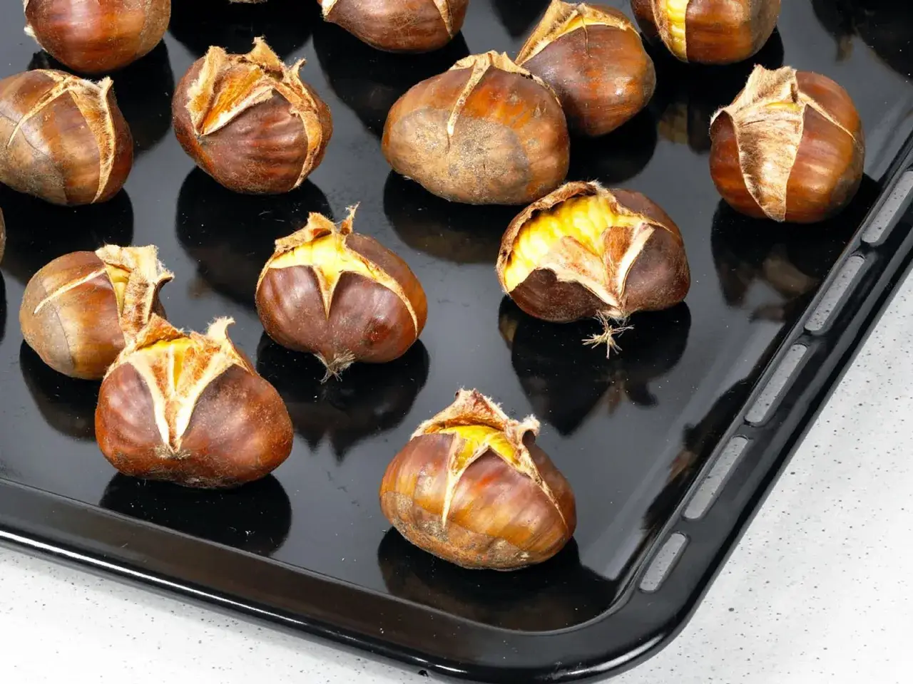 Ger&ouml;stete Maronen auf einem Backblech, bereit zum Genie&szlig;en. Die Schale ist eingeschnitten, um das k&ouml;stliche Innere freizulegen.