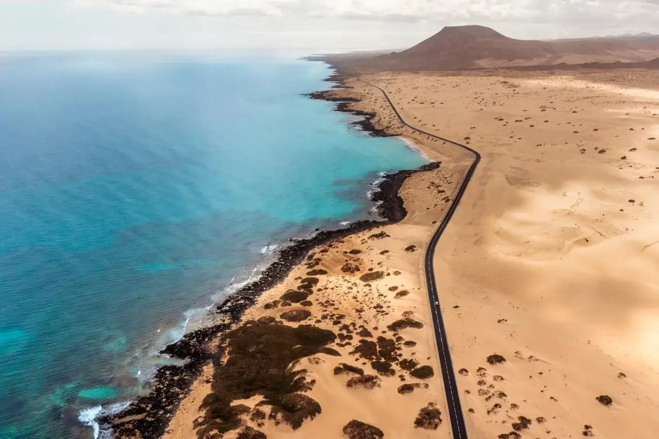 Pustynny krajobraz Fuerteventury z turkusowym oceanem i krętą drogą. Idealne miejsce na zwiedzanie, które inspiruje do stworzenia własnego **fuerteventura plan zwiedzania**.