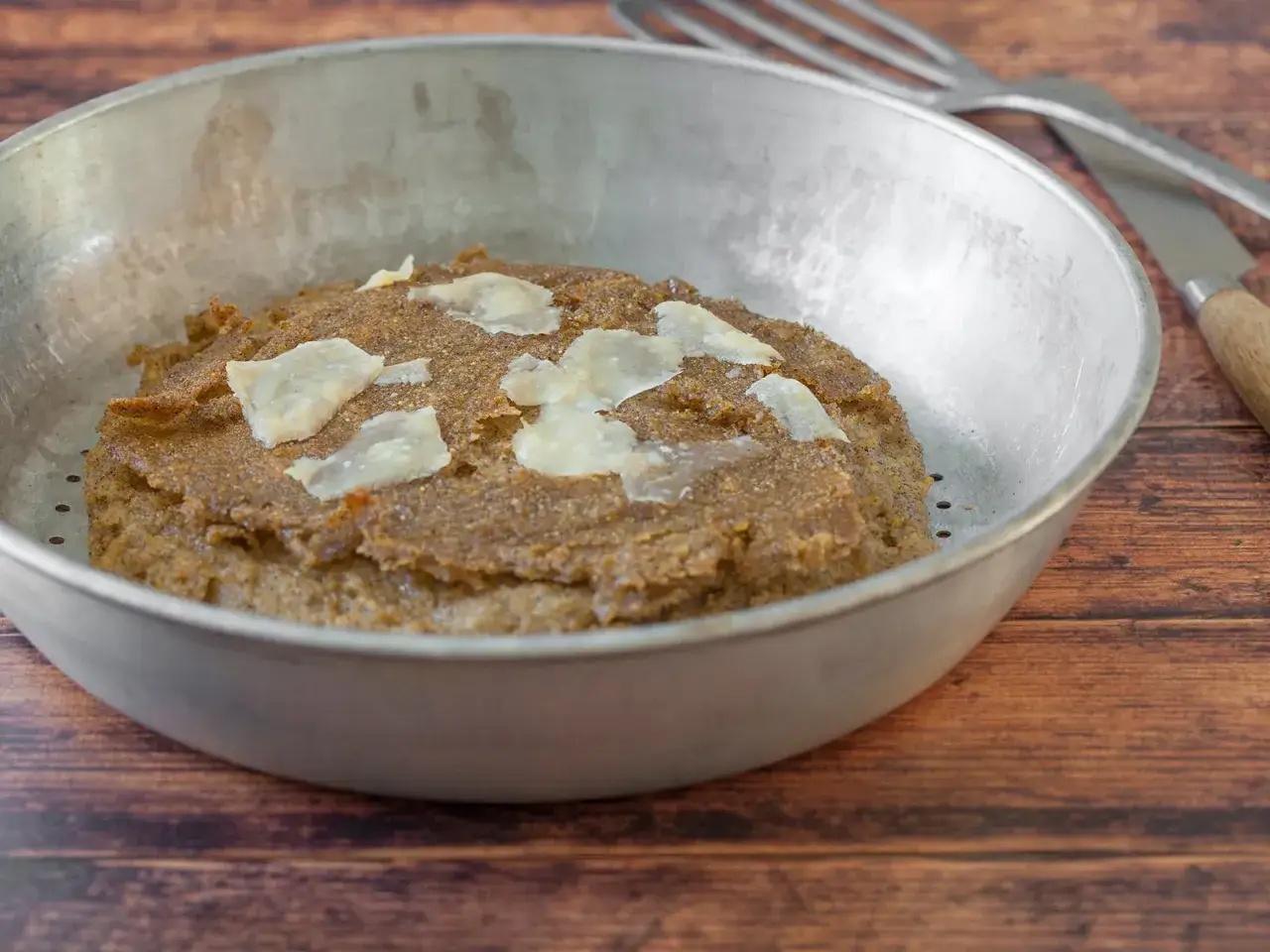 Herzhafte Polenta Taragna, garniert mit K&auml;sesp&auml;nen, in einer Metallsch&uuml;ssel auf Holzhintergrund.