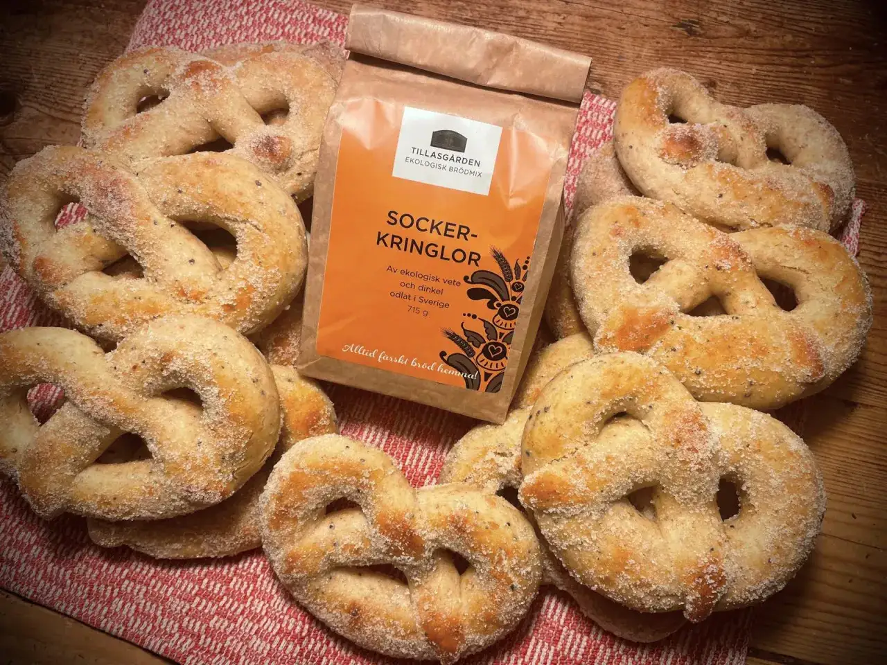 Nybakade socker kringlor, redo att avnjutas. En påse ekologisk brödmix från Tillasgården ligger bredvid, perfekt för att baka med lätta ingredienser.