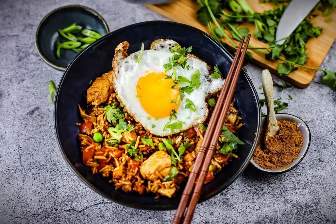 Nasi Goreng: Gebratener Reis mit Hühnchen, Erbsen, Karotten und einem Spiegelei, garniert mit Koriander und Frühlingszwiebeln.
