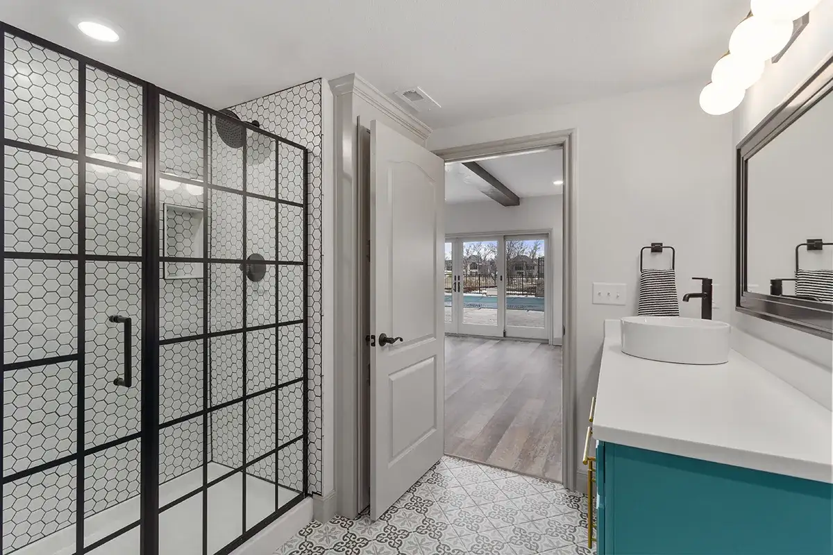 Ba&ntilde;o moderno con ducha de cristal y azulejos hexagonales. La puerta abierta revela una sala con piscina, ideal para como dar luz a una planta baja.