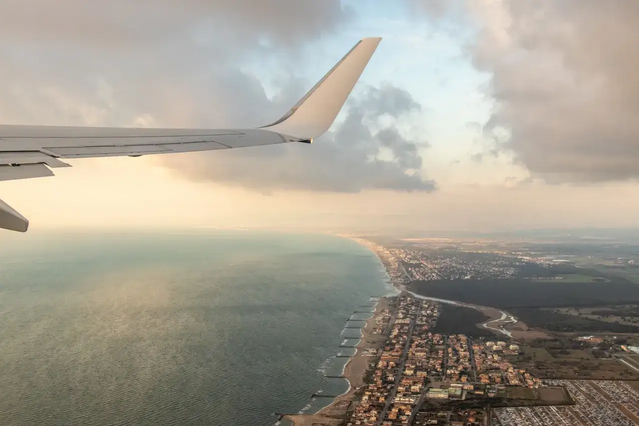 Widok z samolotu na wybrzeże Fiumicino. Skrzydło samolotu, morze i zabudowania wzdłuż plaży.