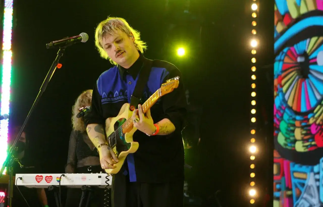 Blazej Król gra na gitarze na scenie, oświetlony kolorowymi światłami.