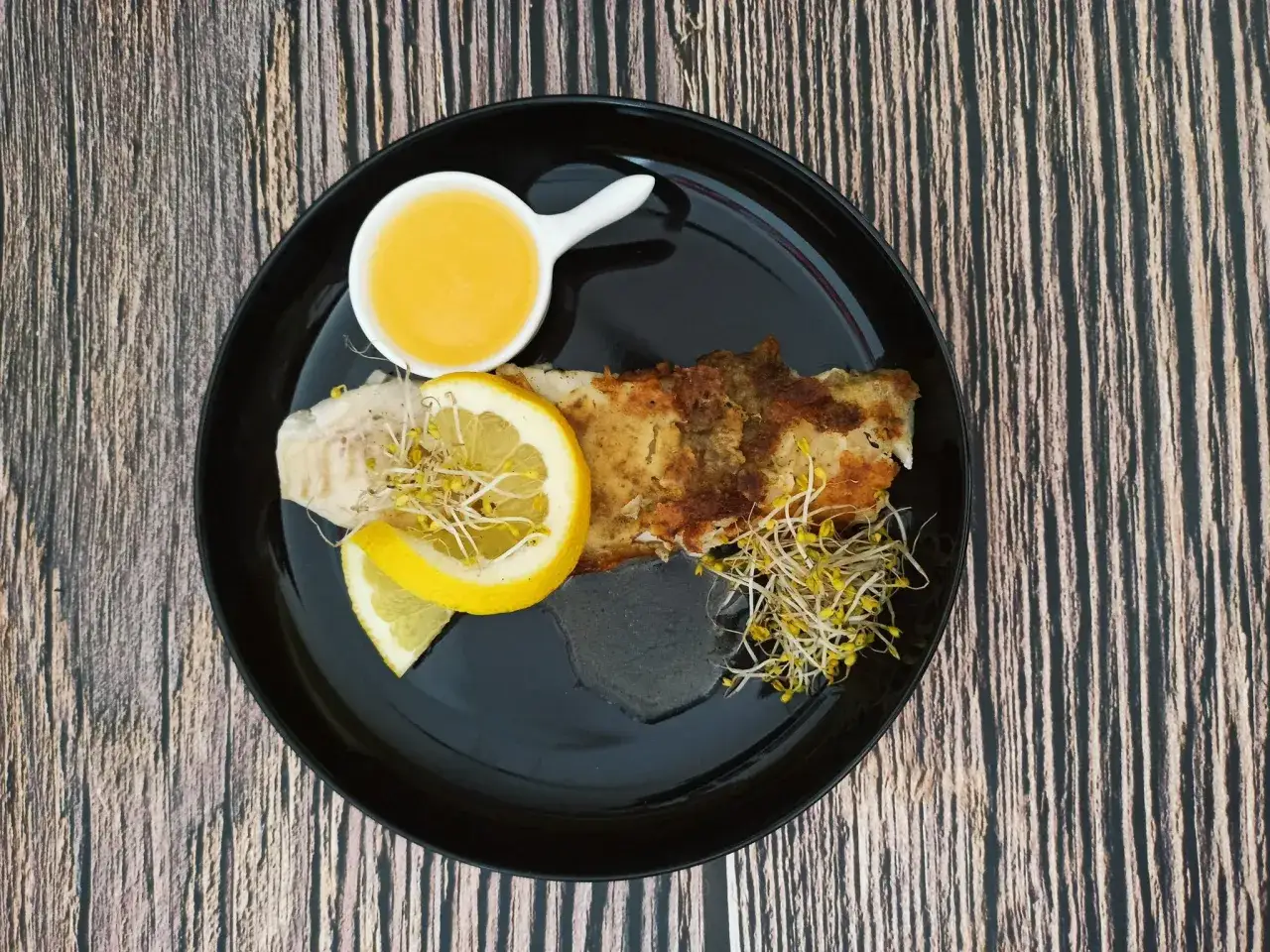Ryba z cytryną i kiełkami, podana z aromatycznym sosem winno maślanym.