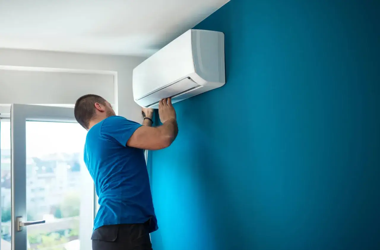 Técnico instalando un aire acondicionado split en una pared azul. Se ve el proceso de como se instala un aire acondicionado.